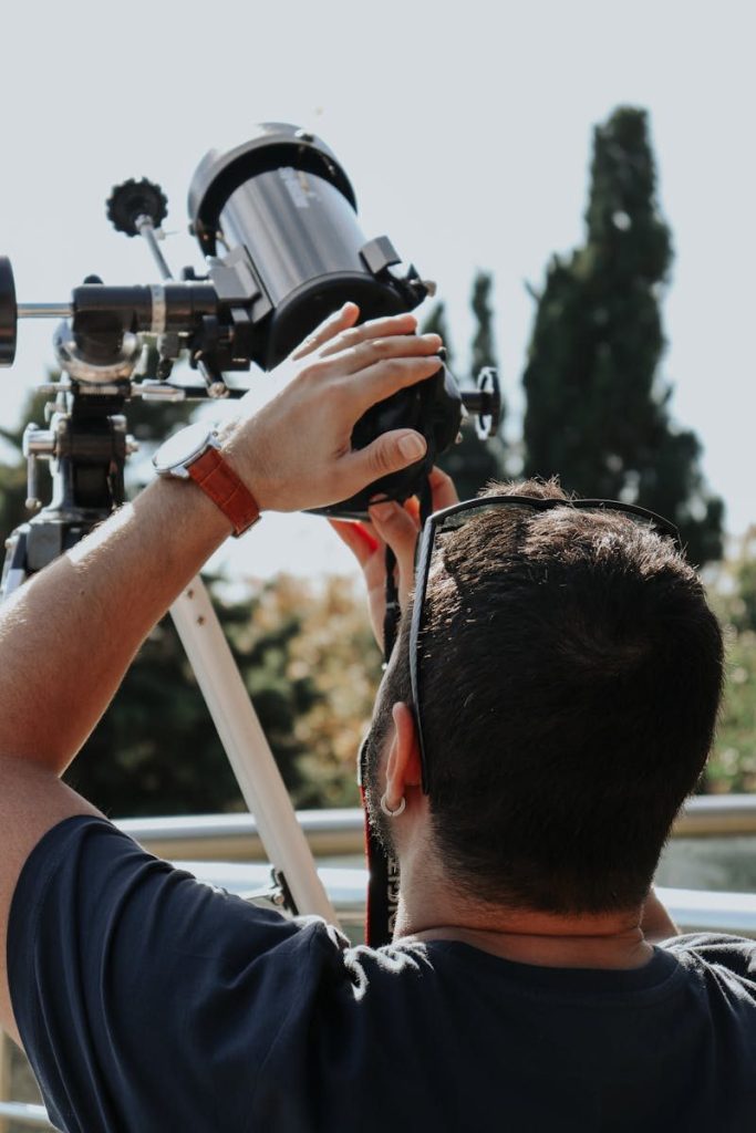 A young man adjusts his telescope outdoors, preparing for a day of stargazing.