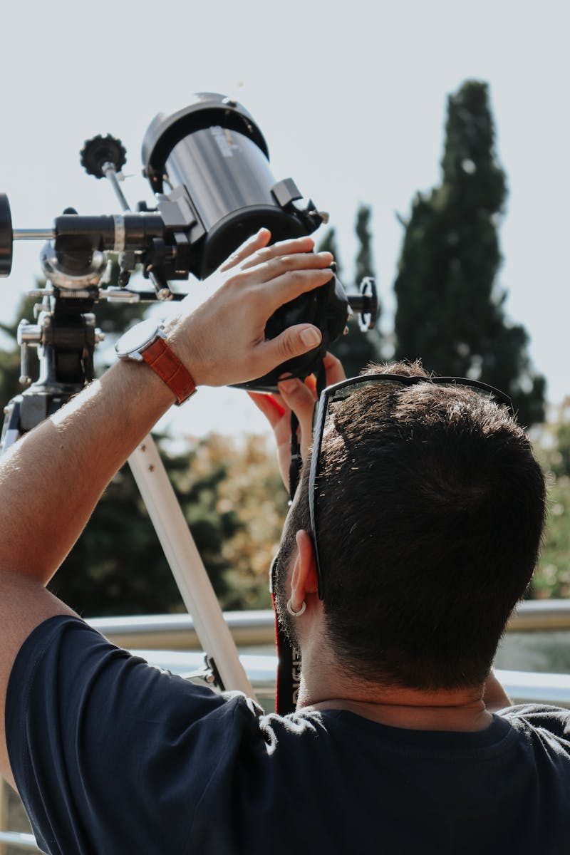 A young man adjusts his telescope outdoors, preparing for a day of stargazing.